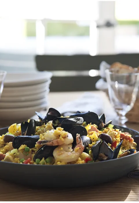 Ina Garten summer paella salad with mussels, shrimp, saffron rice, peppers and peas in a dark serving bowl