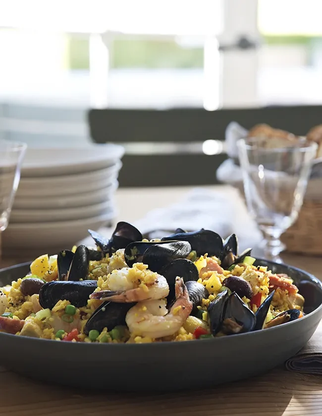 Ina Garten summer paella salad with mussels, shrimp, saffron rice, peppers and peas in a dark serving bowl