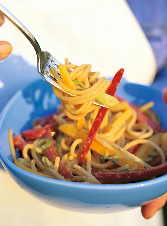 Ina Garten Szechuan noodles twirled on a fork above a blue bowl with red and yellow bell pepper strips and sliced scallions