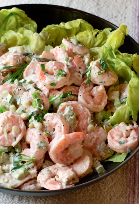 Ina Garten tarragon shrimp salad with pink shrimp, celery and scallions served on butter lettuce leaves in a black bowl