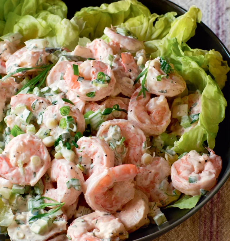 Ina Garten tarragon shrimp salad with pink shrimp, celery and scallions served on butter lettuce leaves in a black bowl
