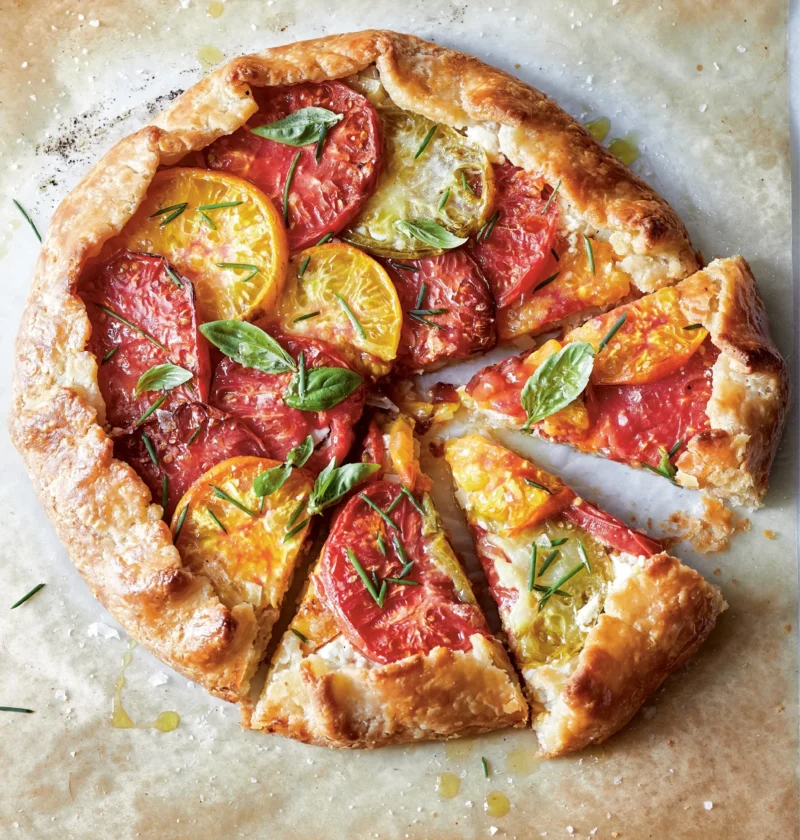 Ina Garten tomato & goat cheese crostata topped with red and yellow heirloom tomato slices and fresh basil on parchment paper