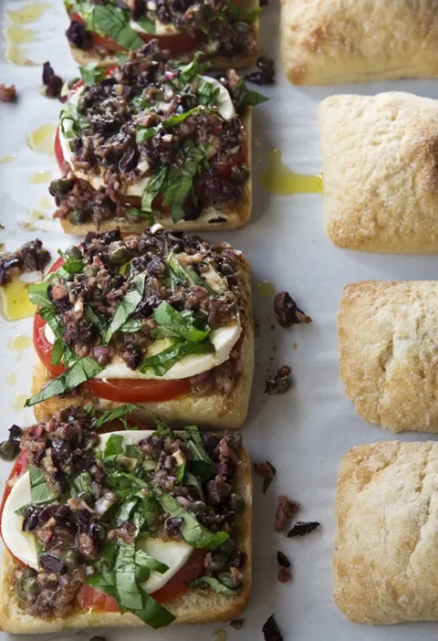 Ina Garten tomato mozzarella pan bagnat open-faced on ciabatta with olive vinaigrette and julienned basil next to toasted ciabatta rolls