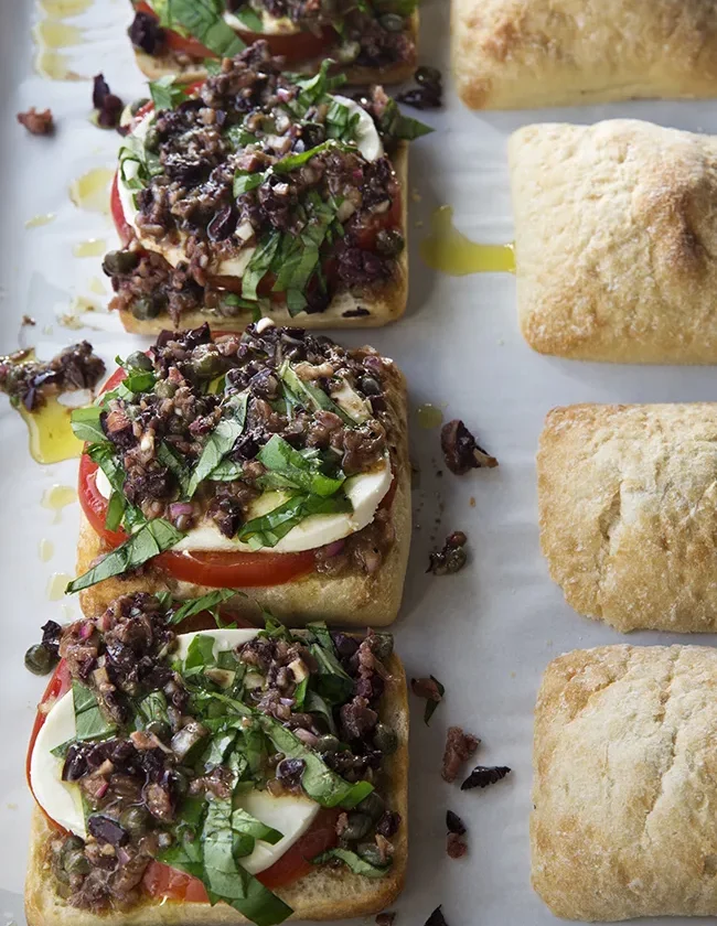 Ina Garten tomato mozzarella pan bagnat open-faced on ciabatta with olive vinaigrette and julienned basil next to toasted ciabatta rolls