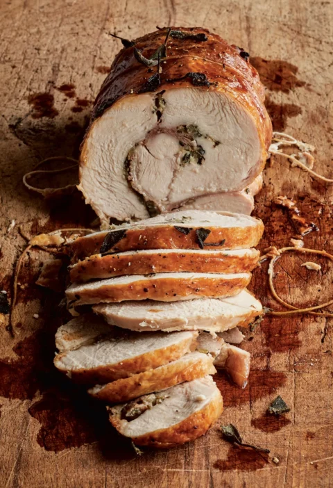 Sliced Ina Garten Tuscan turkey roulade with golden skin, prosciutto, sage and herb filling on a wooden cutting board with kitchen twine