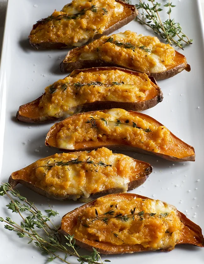 Ina Garten twice-baked sweet potatoes topped with melted Taleggio and fresh thyme sprigs on a white platter