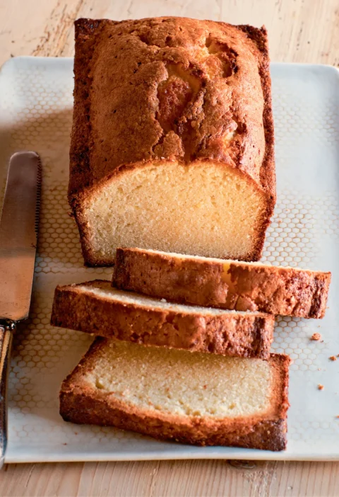 Ina Garten vanilla cream cheese pound cake loaf with three thick slices on a white tray beside a serrated knife