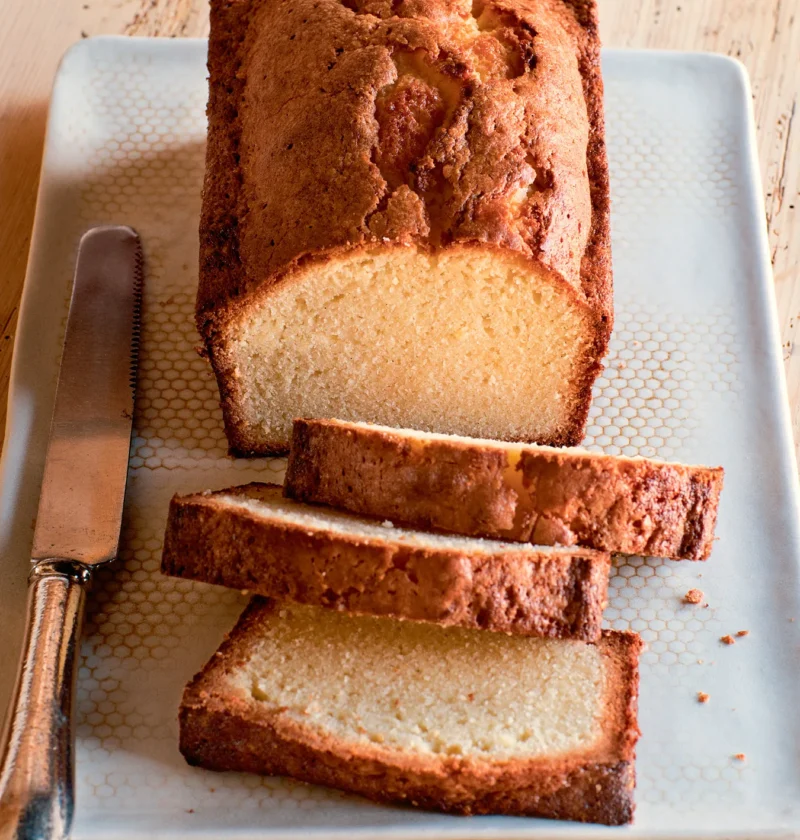 Ina Garten vanilla cream cheese pound cake loaf with three thick slices on a white tray beside a serrated knife