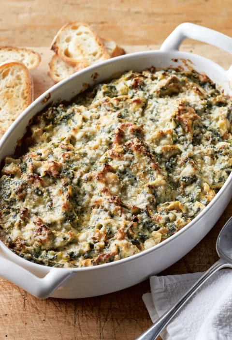 Ina Garten warm spinach & artichoke dip baked golden and bubbly in a white oval dish with toasted baguette slices