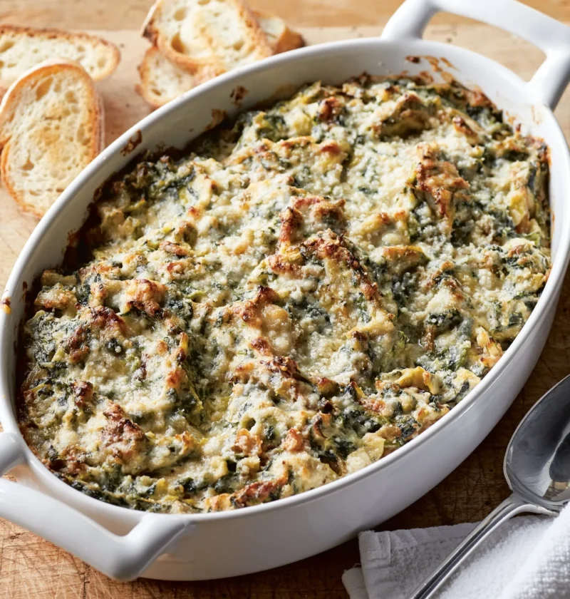 Ina Garten warm spinach & artichoke dip baked golden and bubbly in a white oval dish with toasted baguette slices