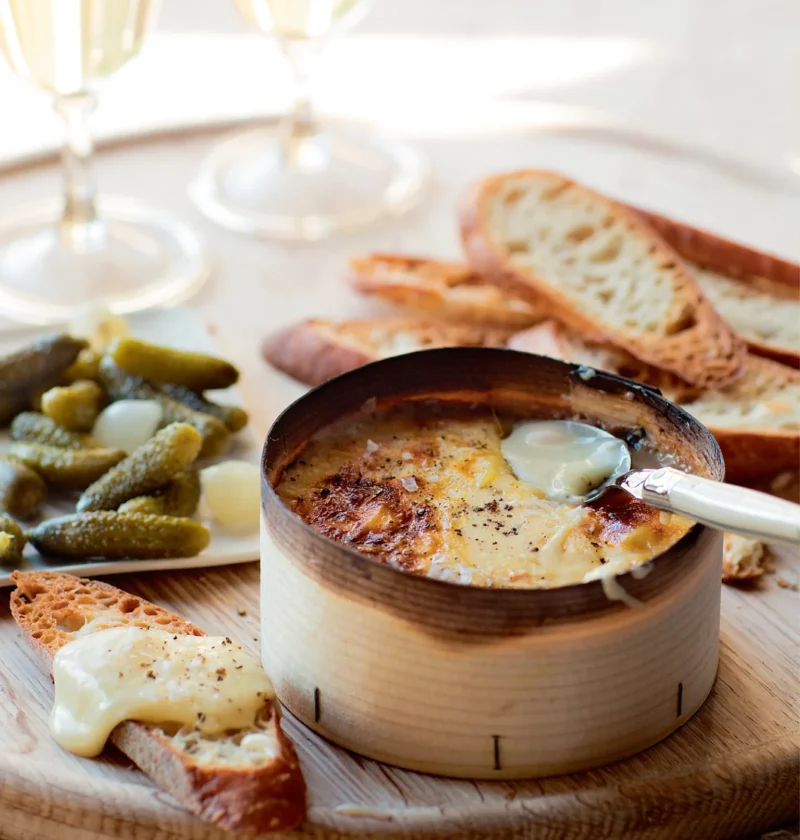 Ina Garten warm vacherin in its wooden box with a spoon, served with toasted bread, cornichons and white wine