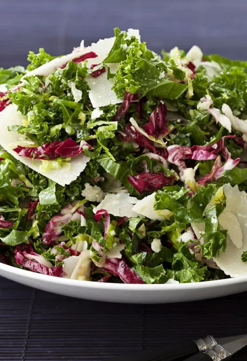 Ina Garten winter slaw with shredded kale, Brussels sprouts, radicchio and Parmesan shavings on a white plate