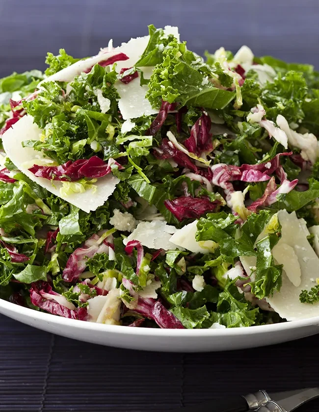 Ina Garten winter slaw with shredded kale, Brussels sprouts, radicchio and Parmesan shavings on a white plate