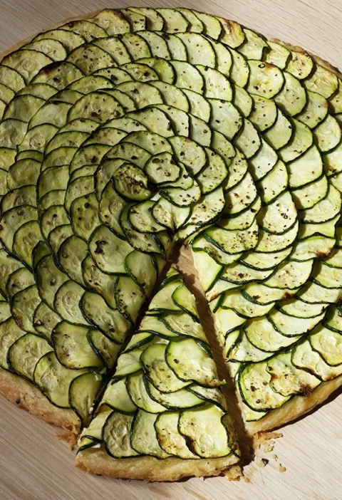 Ina Garten zucchini and goat cheese tart with overlapping spiral rings of zucchini on a golden flaky crust, one wedge cut