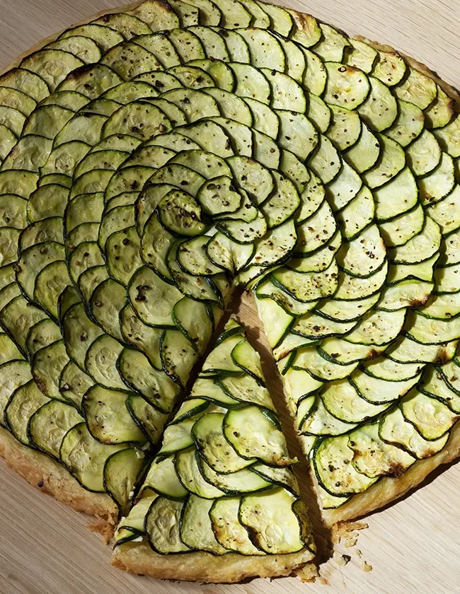 Ina Garten zucchini and goat cheese tart with overlapping spiral rings of zucchini on a golden flaky crust, one wedge cut
