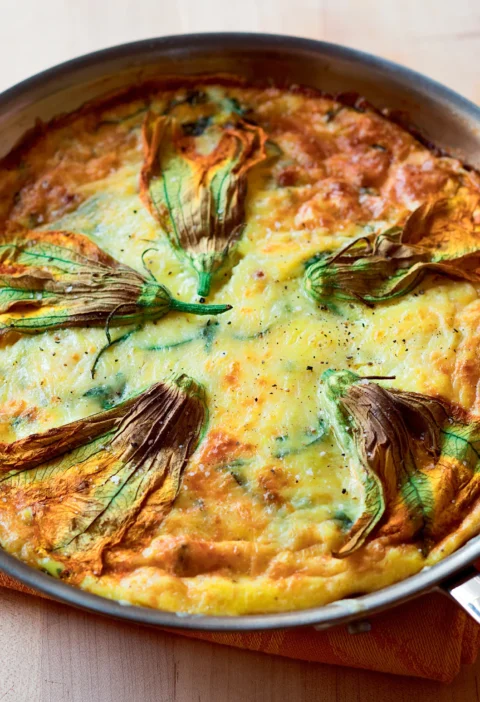 Ina Garten zucchini and leek frittata in a skillet, golden and puffed, decorated with whole zucchini flowers