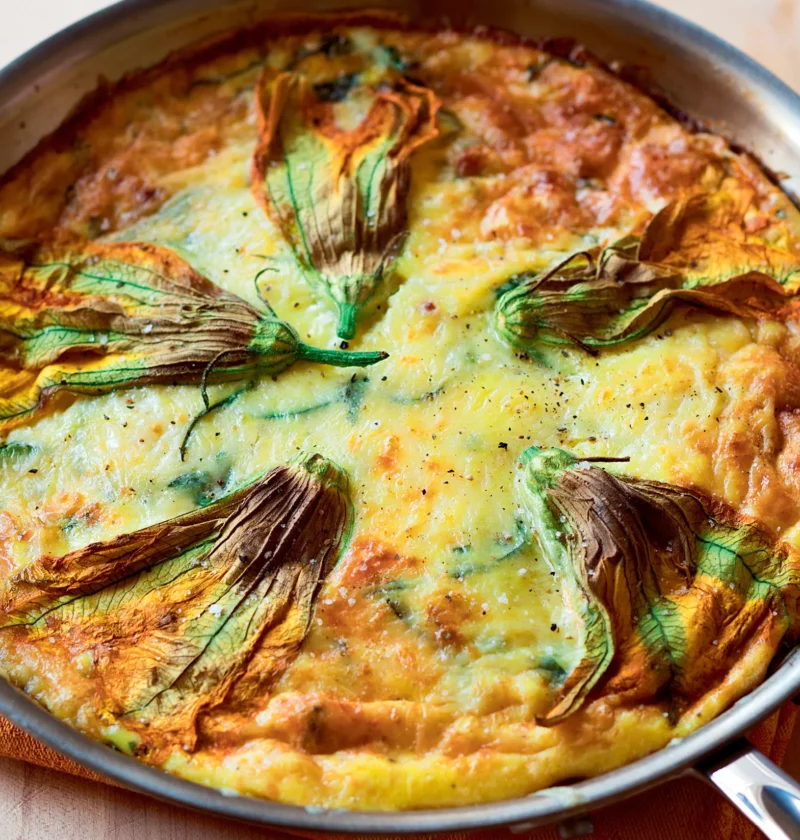 Ina Garten zucchini and leek frittata in a skillet, golden and puffed, decorated with whole zucchini flowers